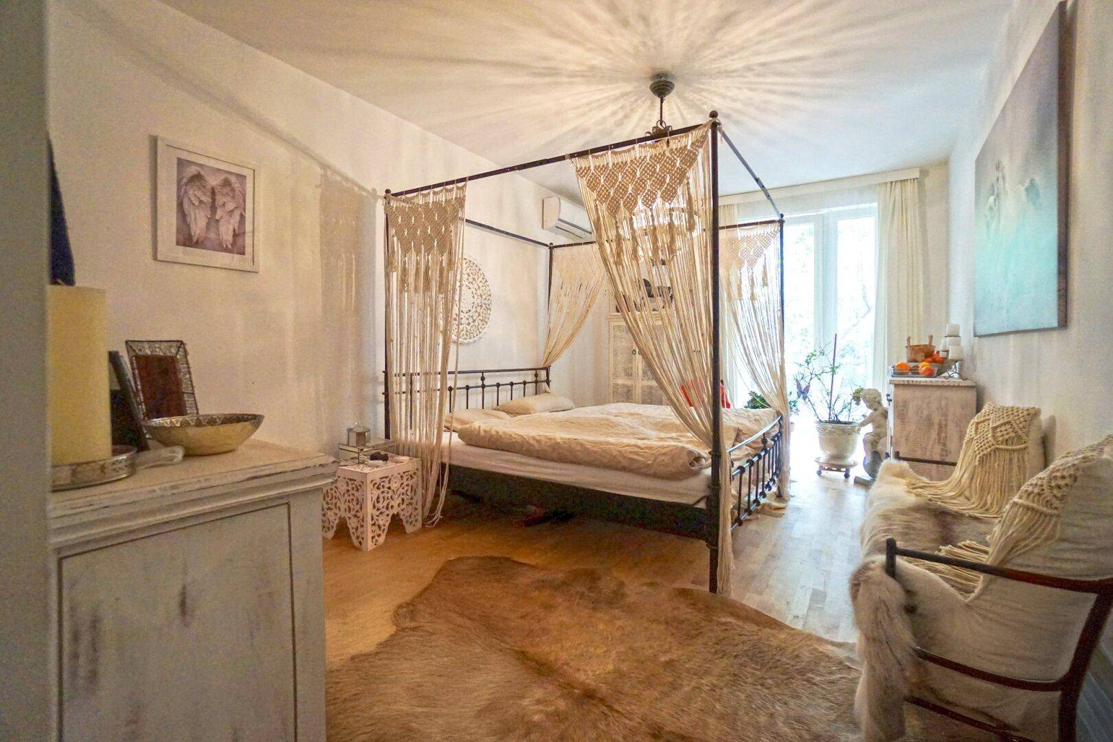 Gemütliches Schlafzimmer mit Himmelbett, Holzboden und Zugang zu einem hellen Außenbereich.