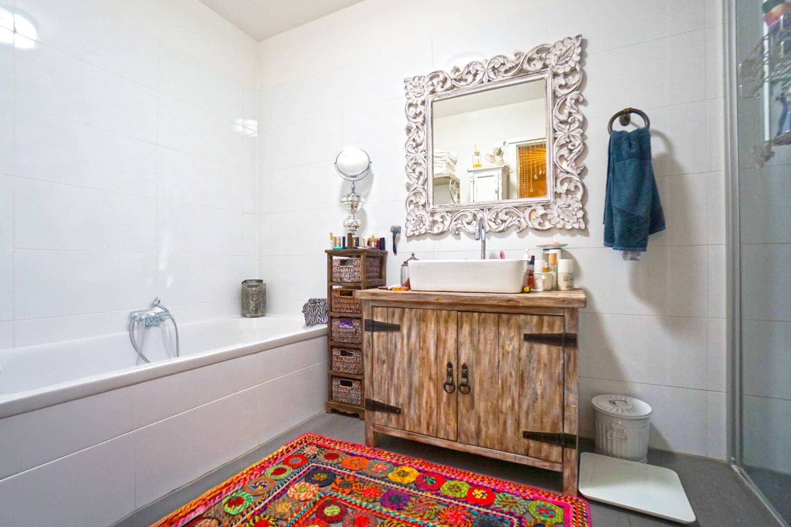 Helles Badezimmer mit Badewanne, modernem Waschtisch und farbenfrohem Teppich.