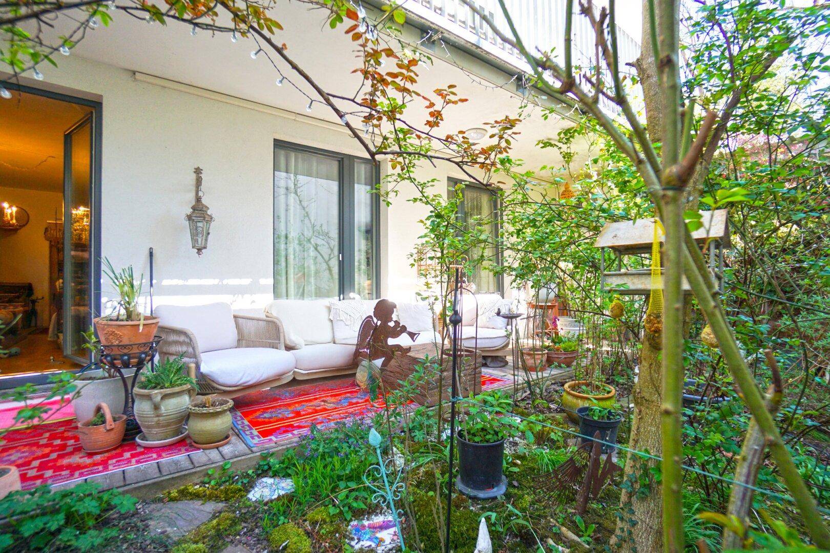 Gemütliche Terrasse mit Sitzgelegenheiten, umgeben von üppigem Grün und Pflanzen.