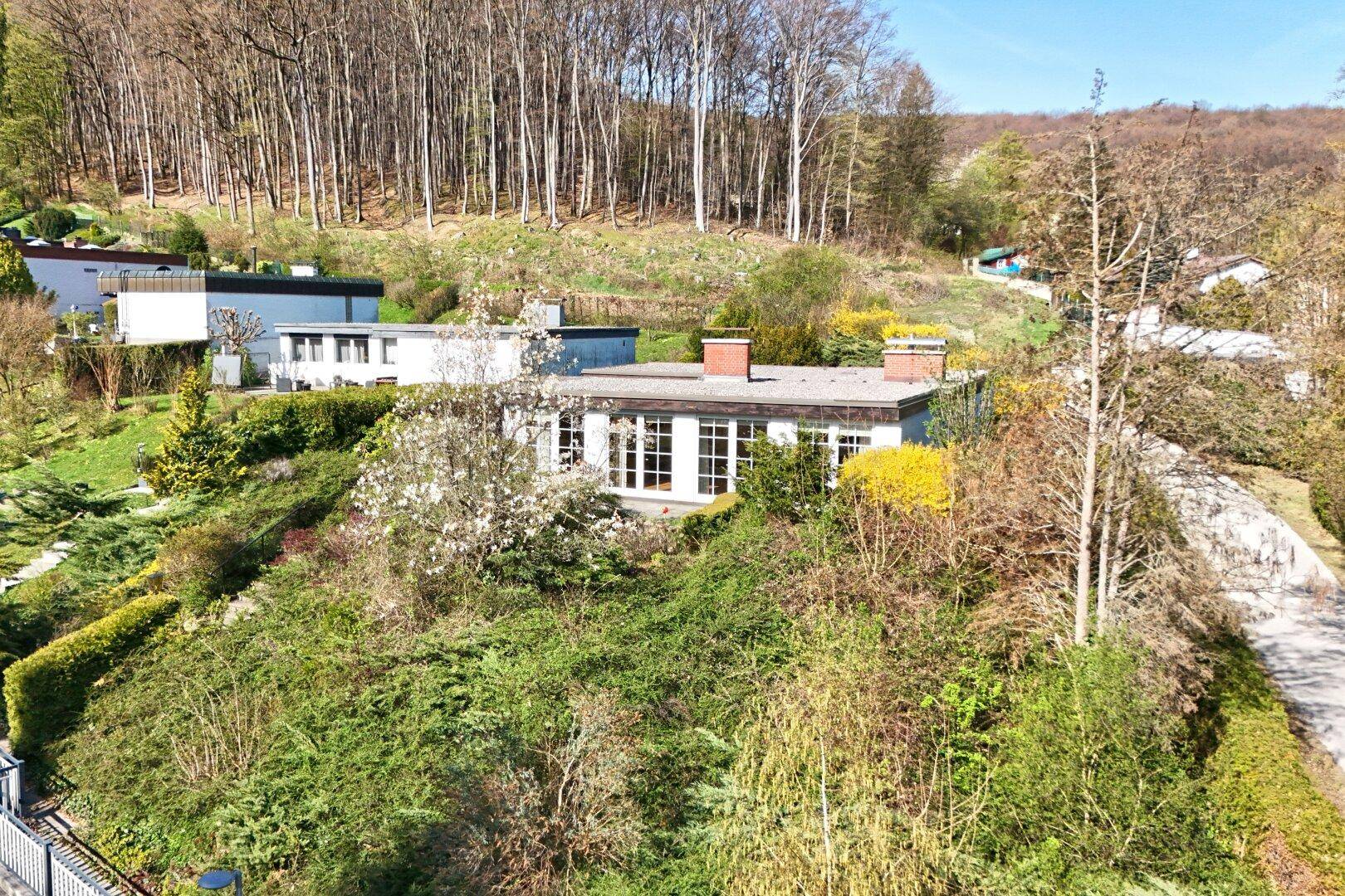 Einfamilienhaus in Hanglage mit weitem Blick auf die umliegende Natur und die bewaldete Hügellandschaft unter blauem Himmel.