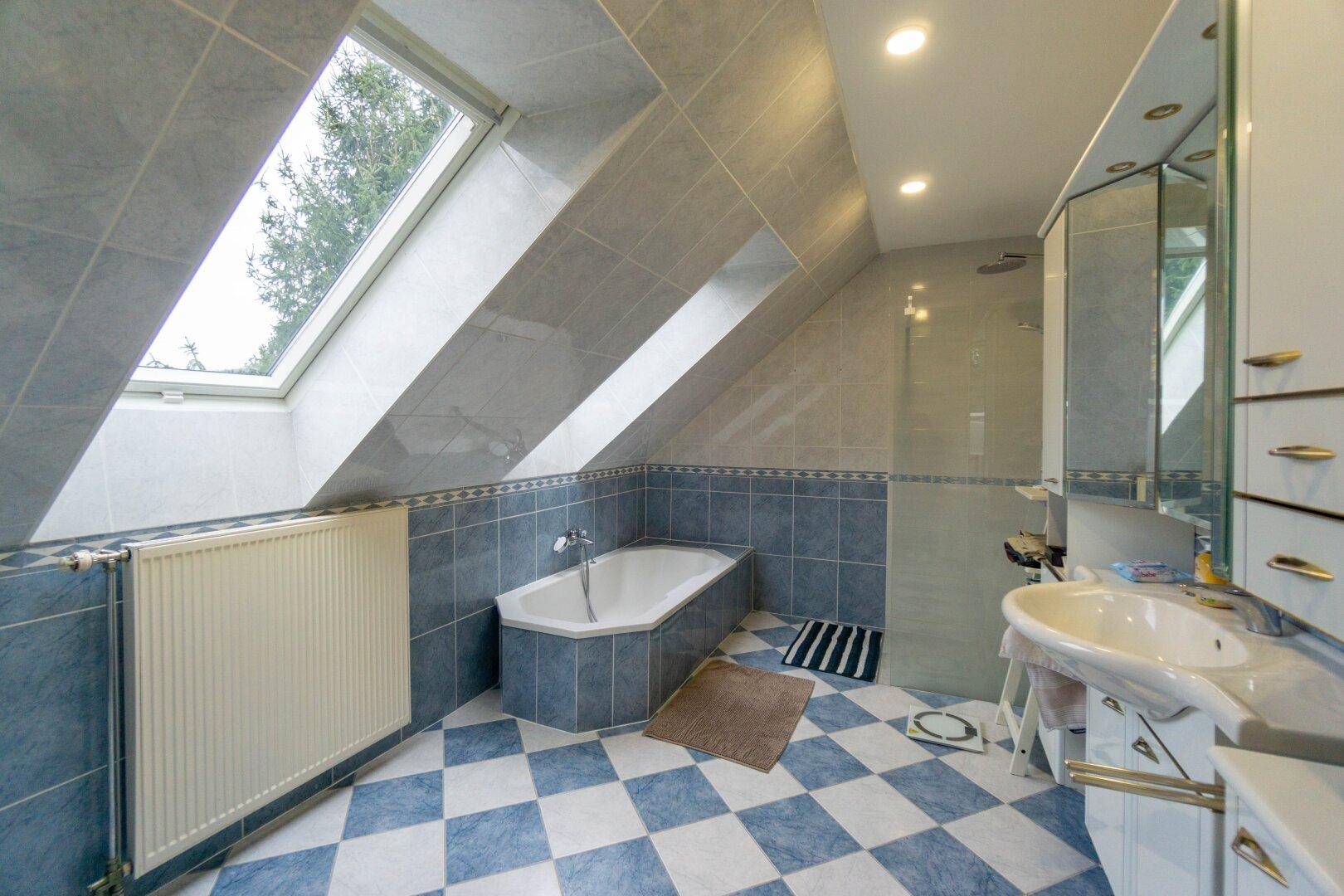 Badezimmer im Dachgeschoss mit Badewanne, Dusche, Dachfenster und blauen Fliesen.