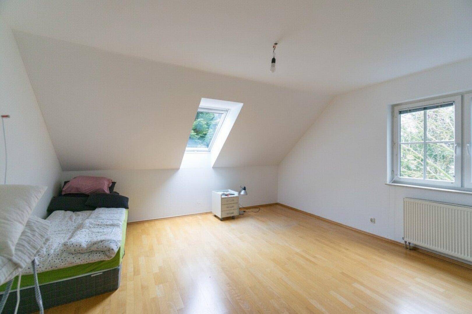 Schlafzimmer im Dachgeschoss mit Parkettboden, Dachfenster und Blick ins Grüne.