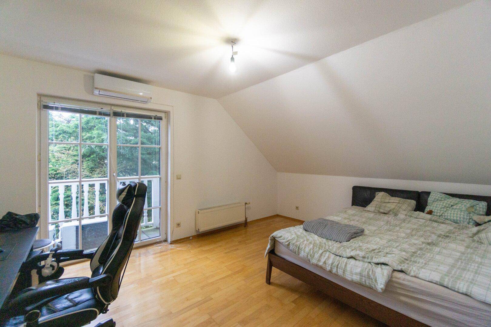 Schlafzimmer im Dachgeschoss mit Parkettboden, Klimaanlage und Balkonzugang.
