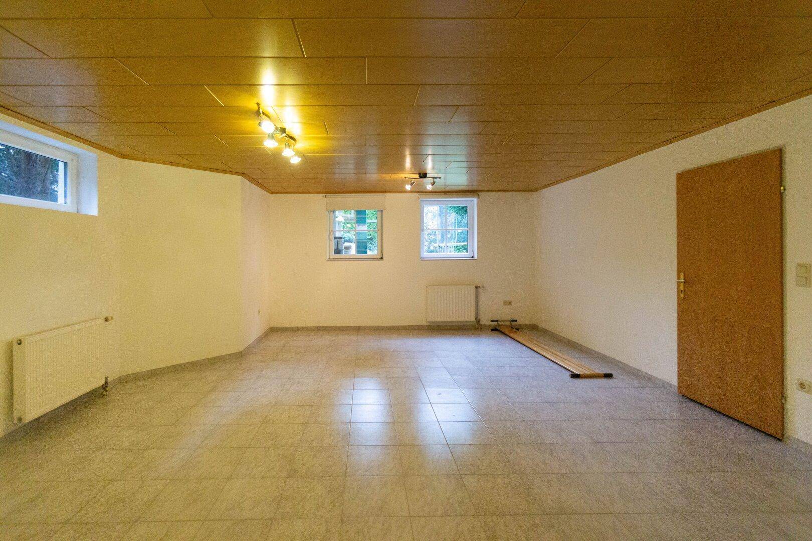 Geräumiger Raum im Untergeschoss mit Fliesenboden und Holzdecke.