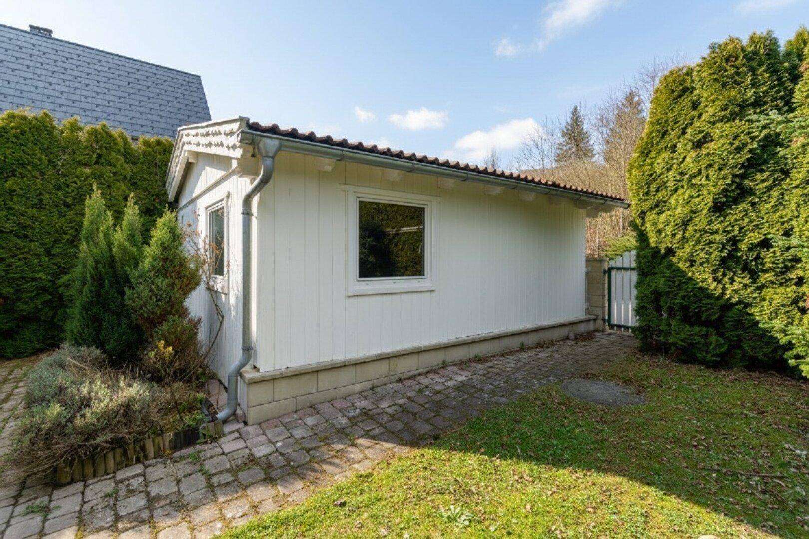 Kleines Gartenhaus mit Fenstern und gepflastertem Weg im Grünen.