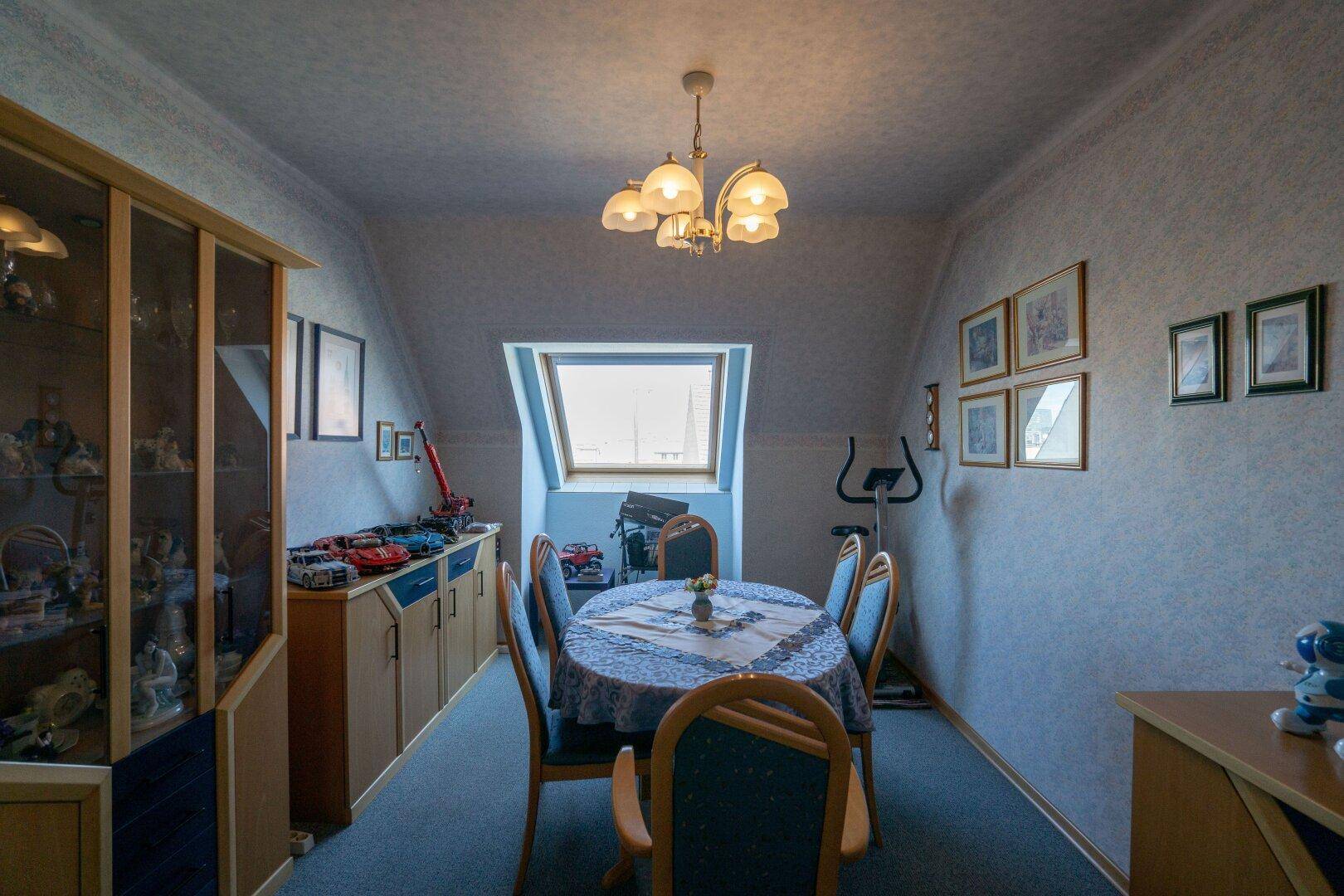 Esszimmer unter der Dachschräge mit Teppichboden, Dachfenster und Vitrine für Geschirr.