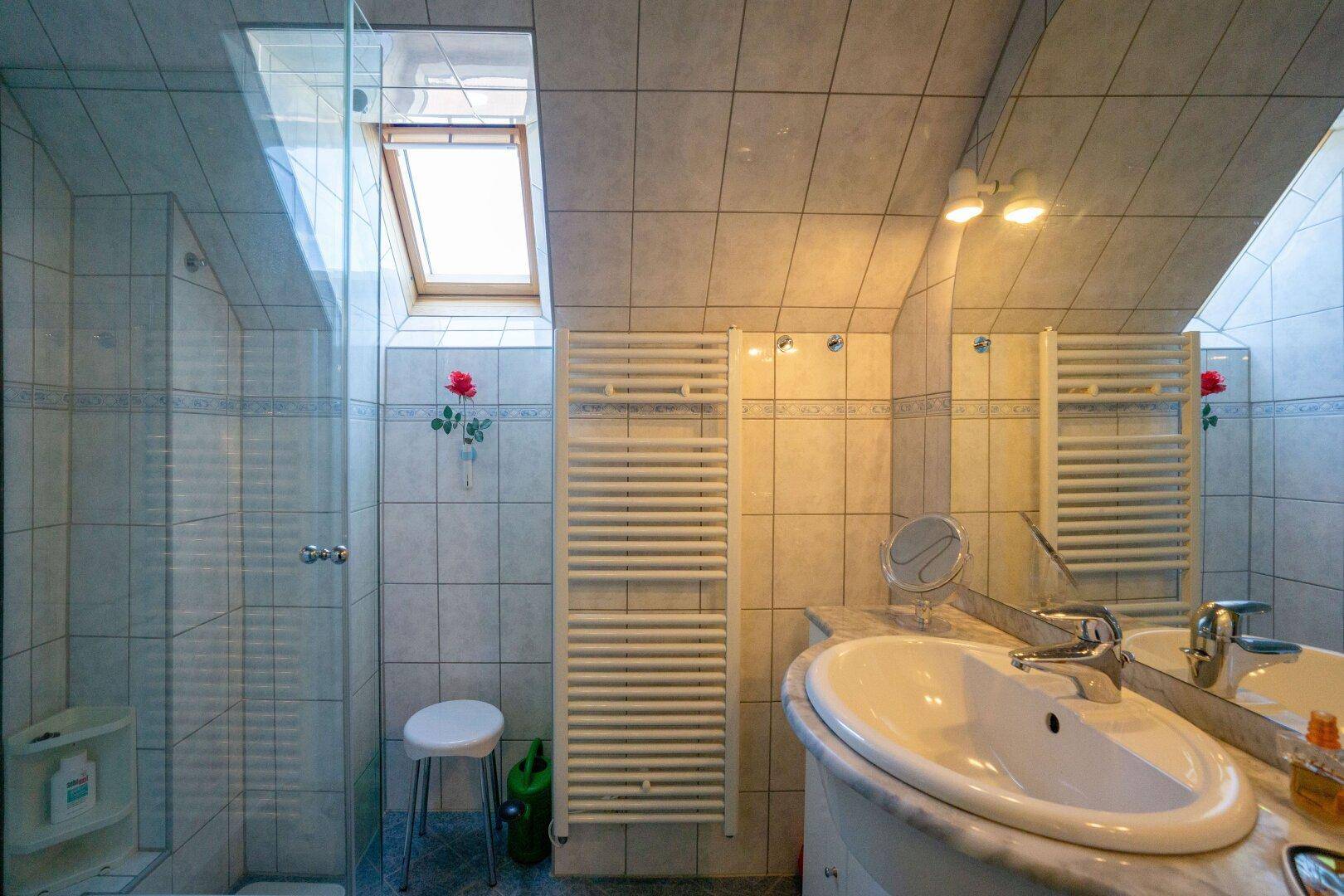 Gefliestes Badezimmer mit Dachfenster, Duschkabine und Waschbecken unter der Dachschräge.