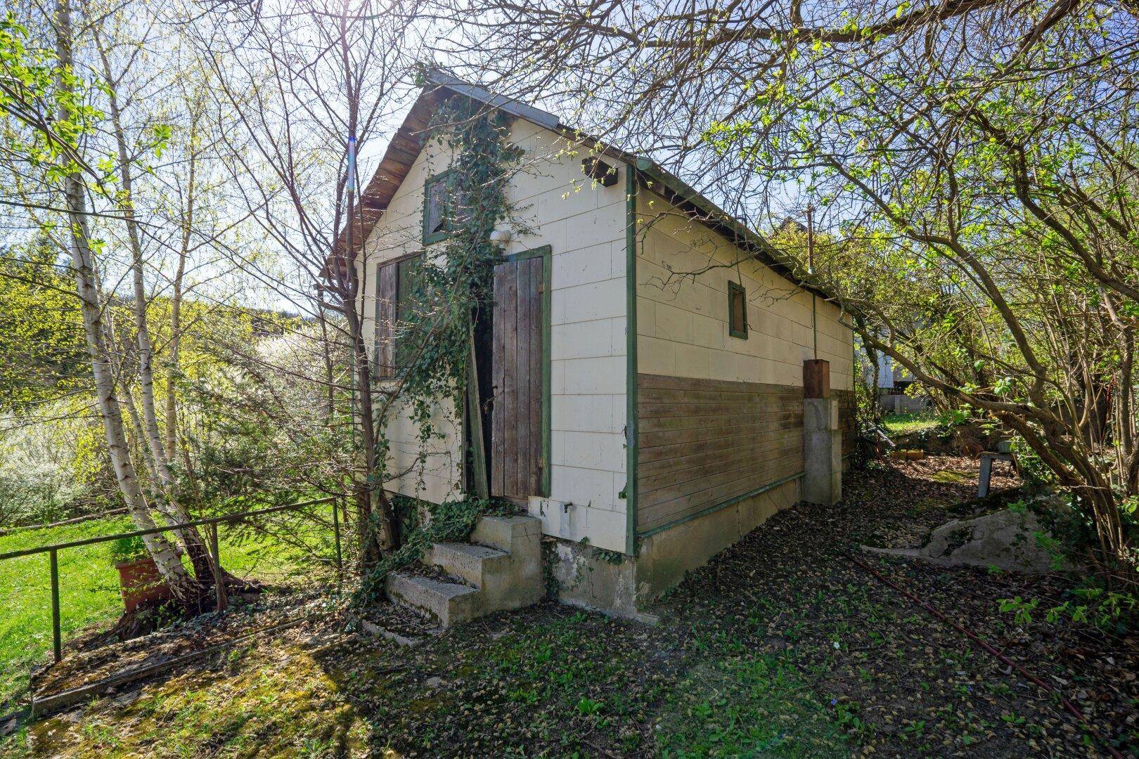 Kleiner, rustikaler Gartenschuppen mit Holztüren und bewachsenen Wänden in ländlicher Umgebung.