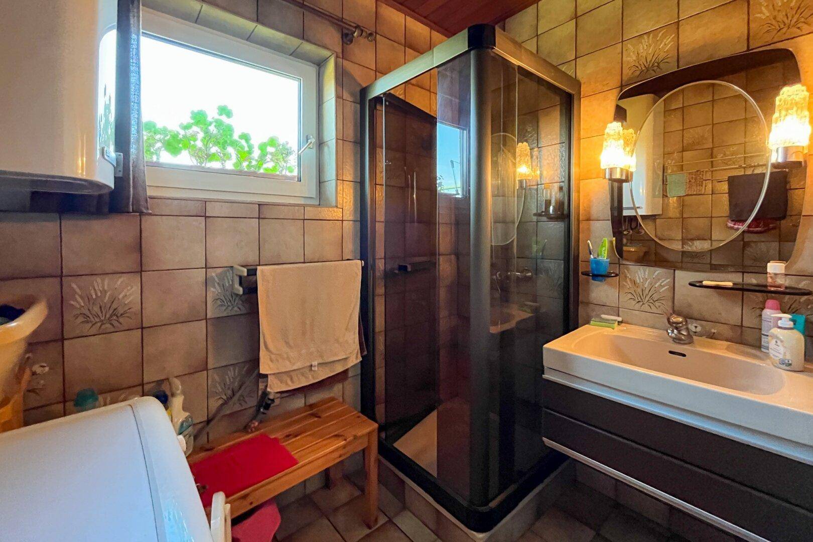 Gefliestes Badezimmer mit Duschkabine, Waschbecken und Fenster für Tageslicht.