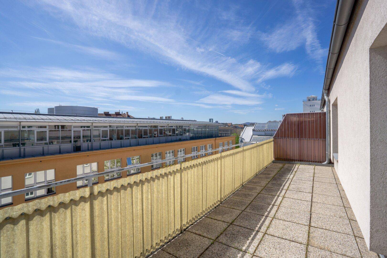 Geräumige Dachterrasse mit Fliesenboden und weitem Blick über die Stadt und umliegende Gebäude.
