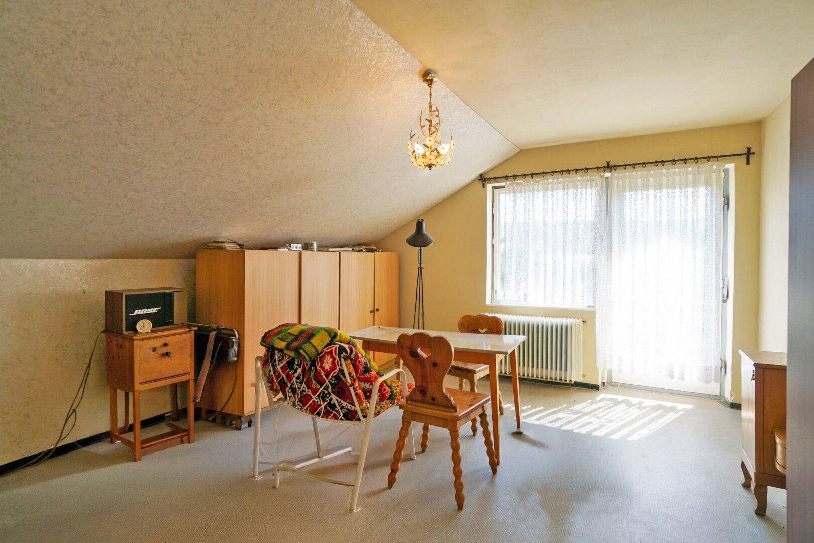 Dachgeschoss-Schlafzimmer mit viel Tageslicht, schrägen Wänden und einfacher Möblierung.
