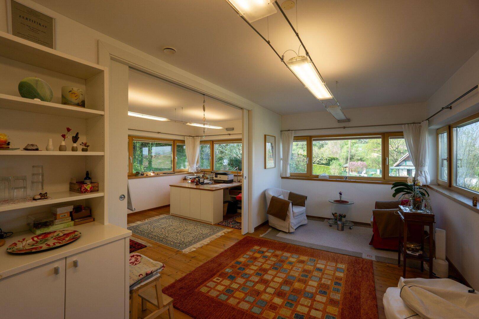 Geräumiges Büro mit vielen Fenstern, Holzboden und Blick auf die grüne Umgebung.