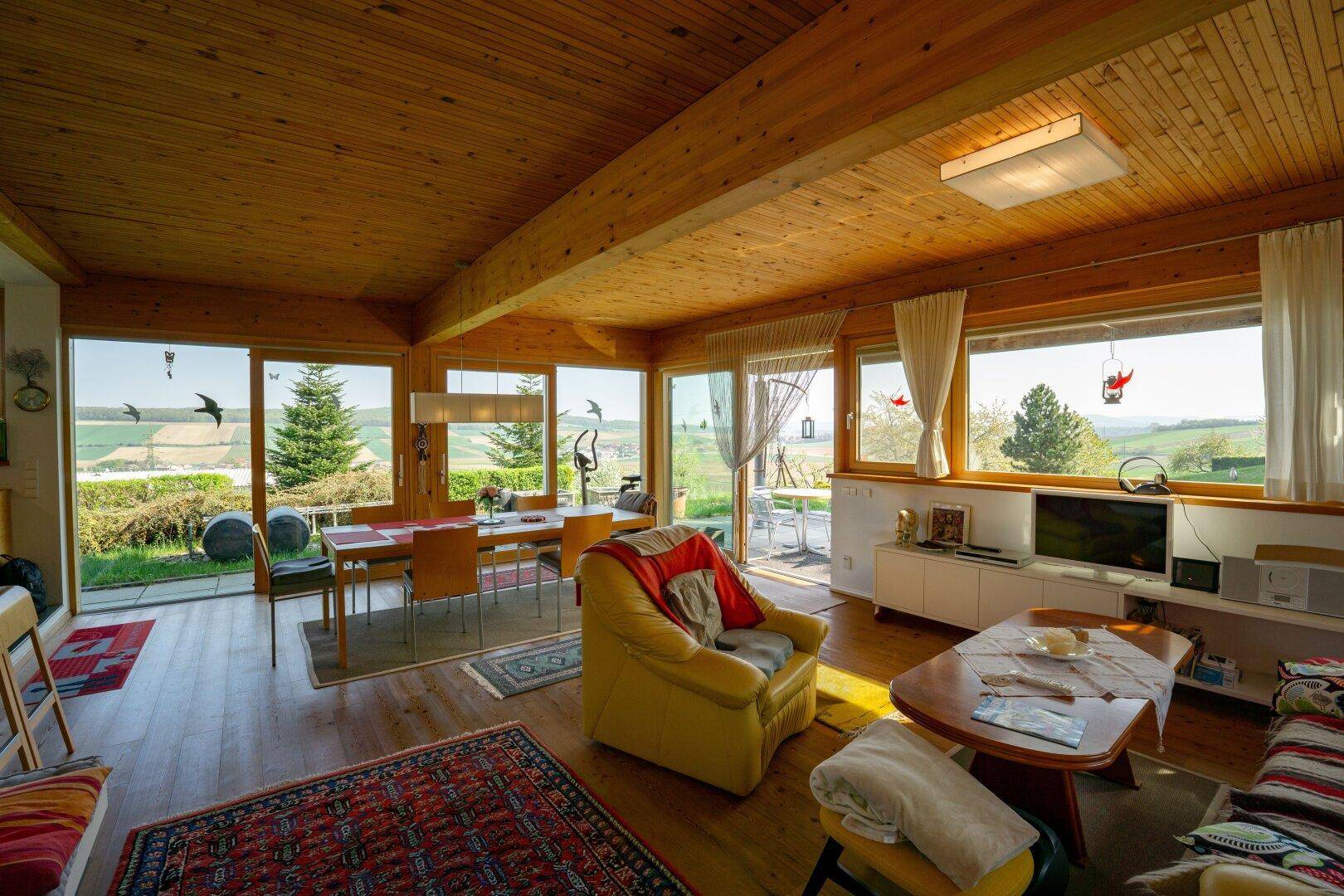 Lichtdurchfluteter Wohn-Essbereich mit Holzbalkendecke, großen Fenstern und Zugang zur Terrasse.