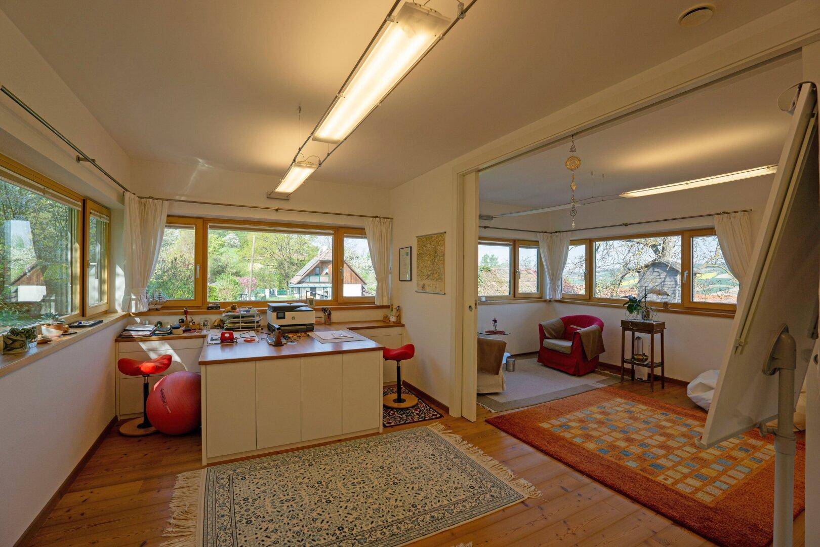 Helles Arbeitszimmer mit mehreren Fenstern, Holzboden und Blick auf die Natur.
