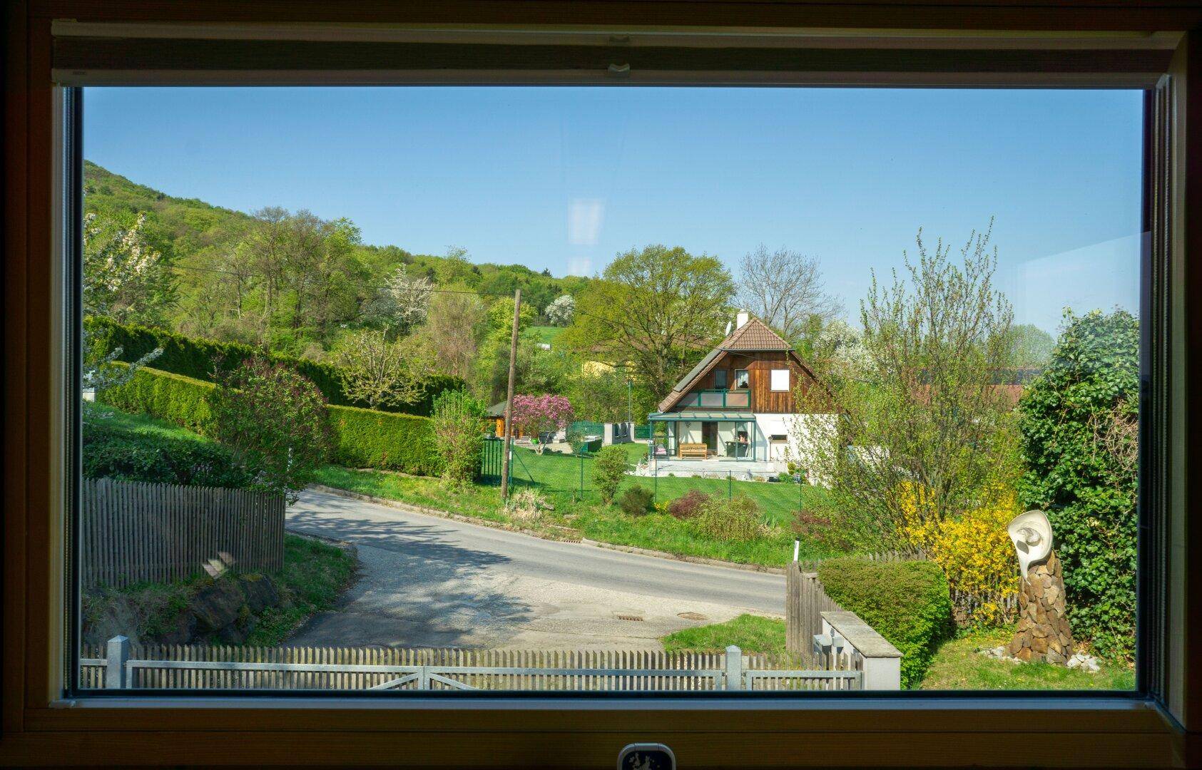 Ausblick aus einem Fenster auf ein Nachbarhaus und die grüne Hügellandschaft.