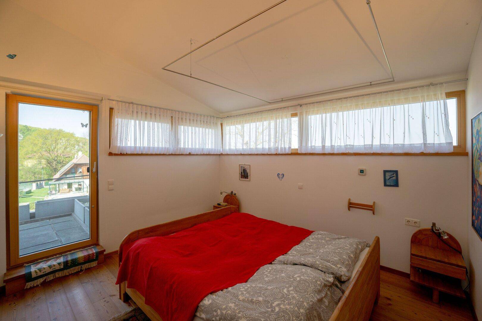 Schlafzimmer mit Holzboden, großen Fenstern und Zugang zu einer Dachterrasse.