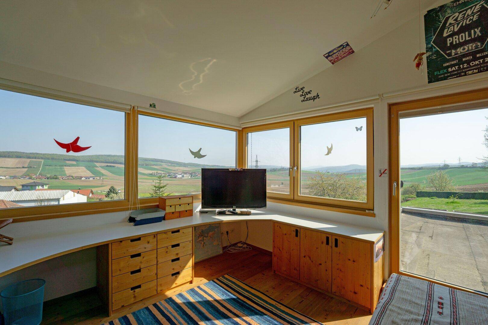 Helles Schlafzimmer mit Eckfenstern, Holzboden und Schreibtisch mit weitem Landschaftsblick.
