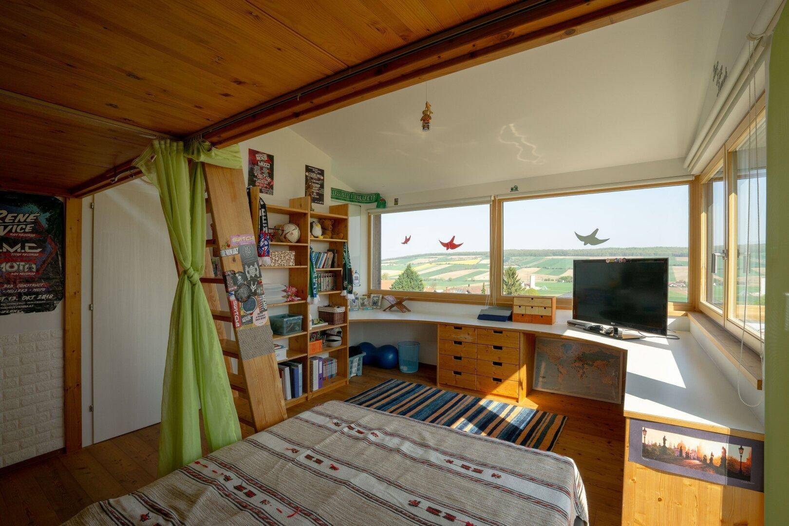 Gemütliches Schlafzimmer mit Holzboden, Bücherregal und großen Fenstern mit Landschaftsblick.