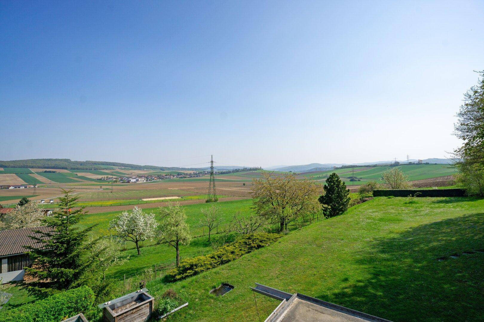Panoramablick über die weiten Felder und die grüne, hügelige Landschaft unter blauem Himmel.