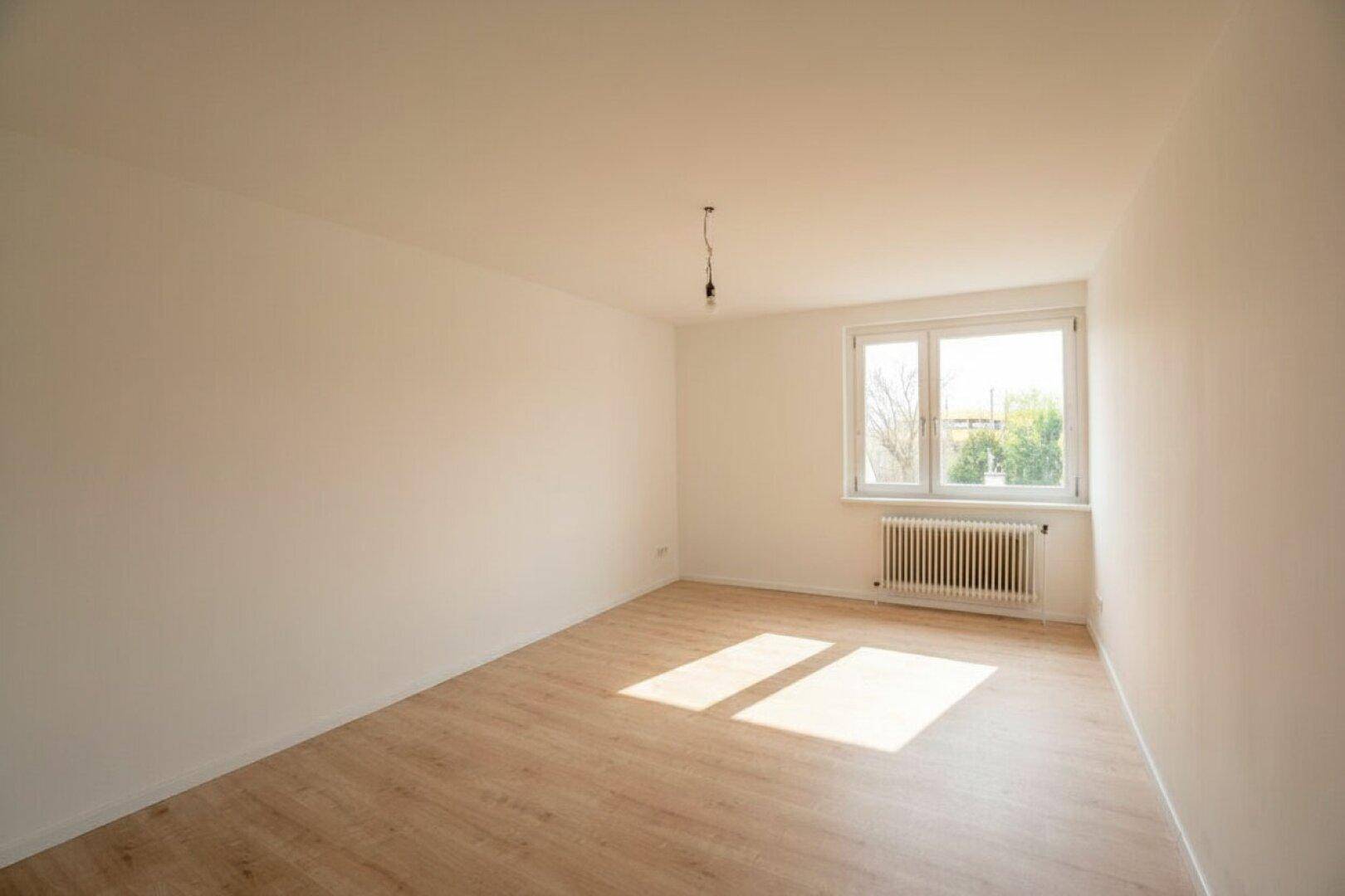 Helles, unmöbliertes Zimmer mit Laminatboden und Fenster, das viel Tageslicht hereinlässt.