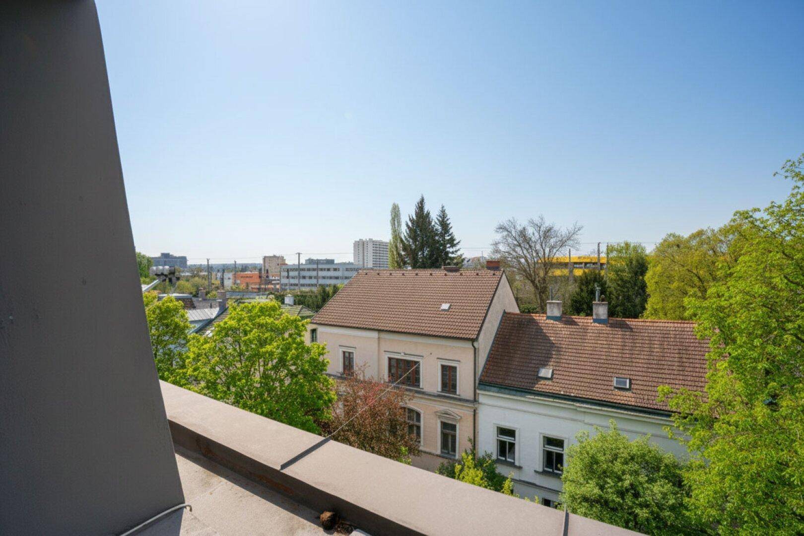 Weitblick über die Dächer der Stadt mit grünen Bäumen und blauem Himmel.
