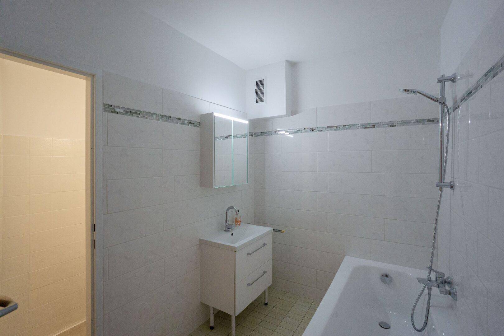 Helles Badezimmer mit Badewanne, Waschbecken und weißen Fliesen an den Wänden.