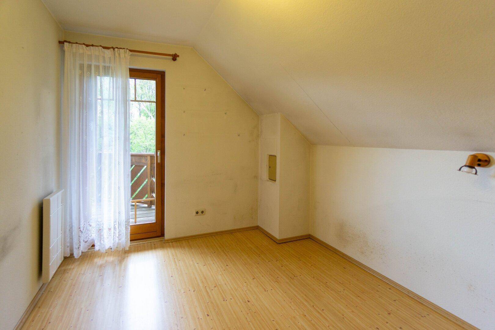 Zimmer mit Laminatboden, Dachschräge und Zugang zu einem kleinen Balkon.