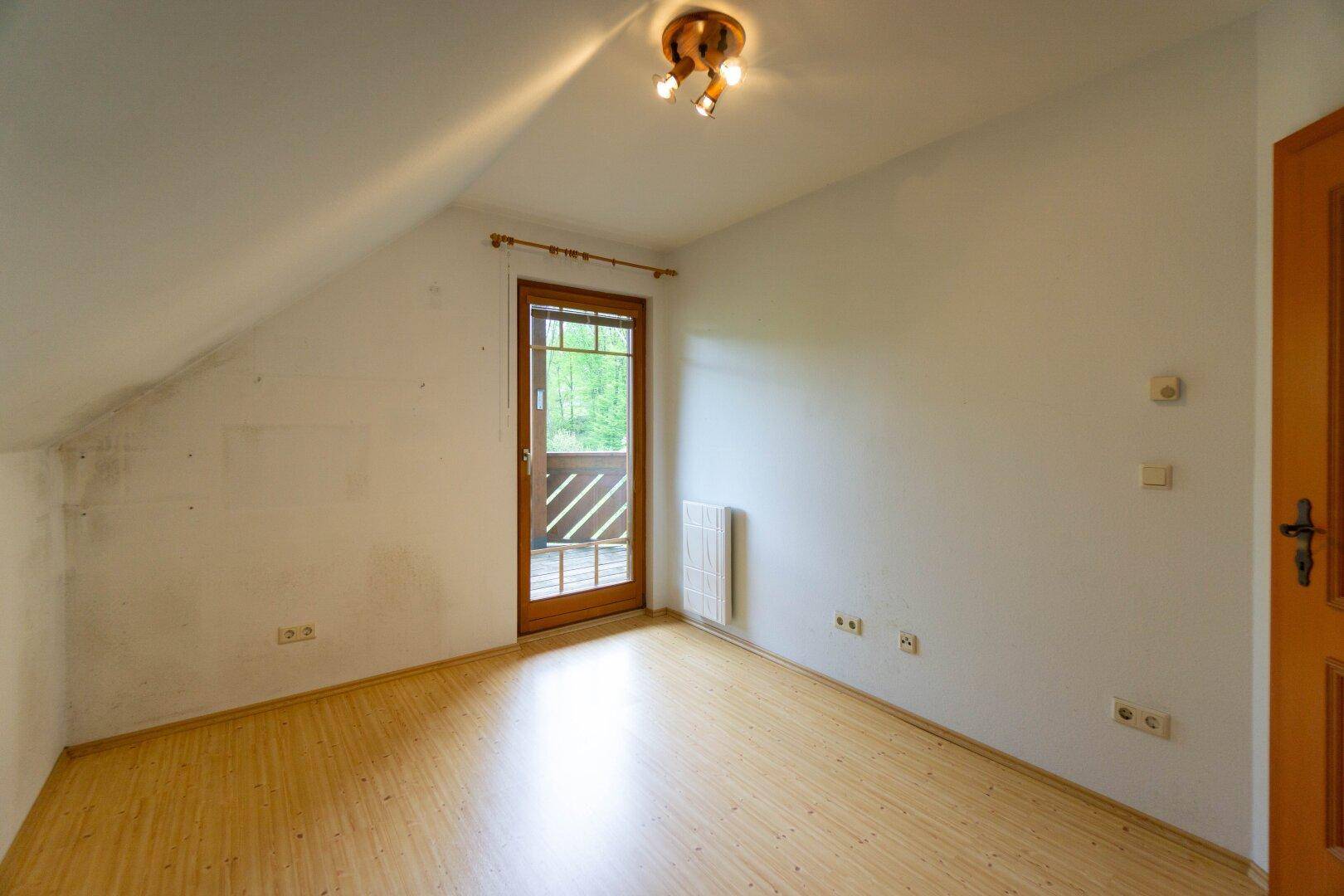Weiteres Zimmer mit Laminatboden, Dachschräge und Zugang zum Balkon.