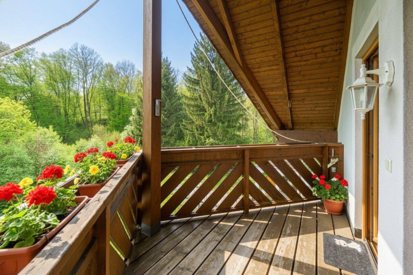 Überdachter Holzbalkon mit Blumenkästen und idyllischem Waldblick.