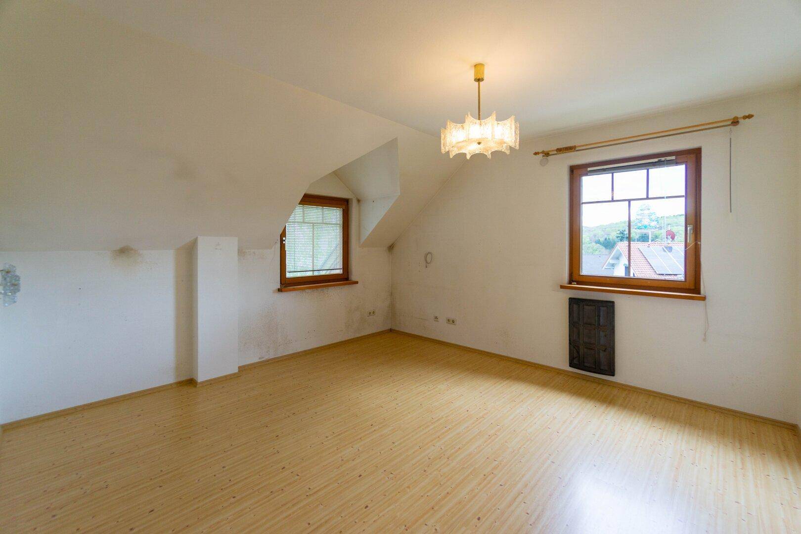 Helles Zimmer im Dachgeschoss mit Laminatboden und zwei Fenstern.