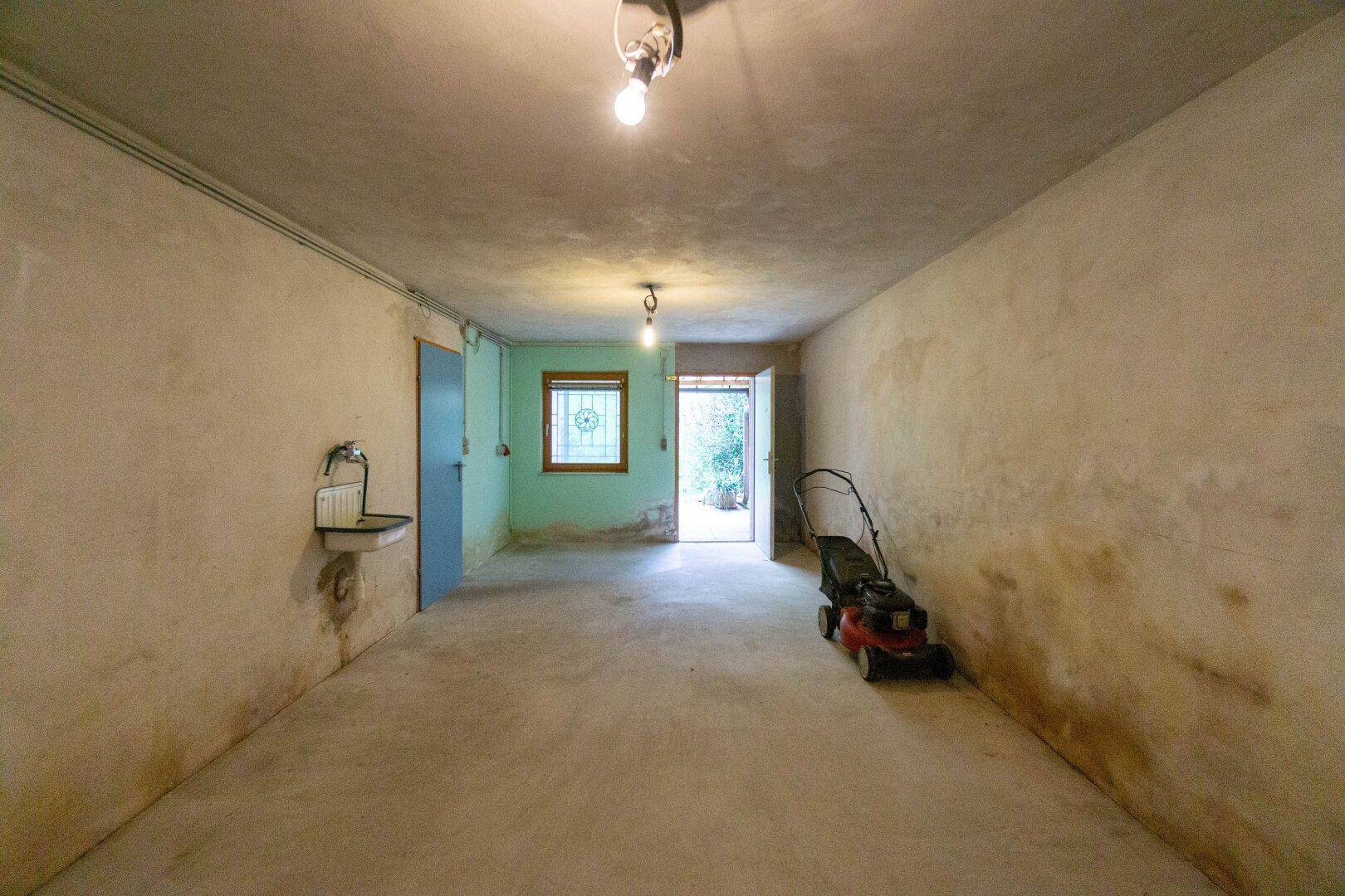 Geräumiger Kellerraum mit Betonboden und Zugang zum Garten.