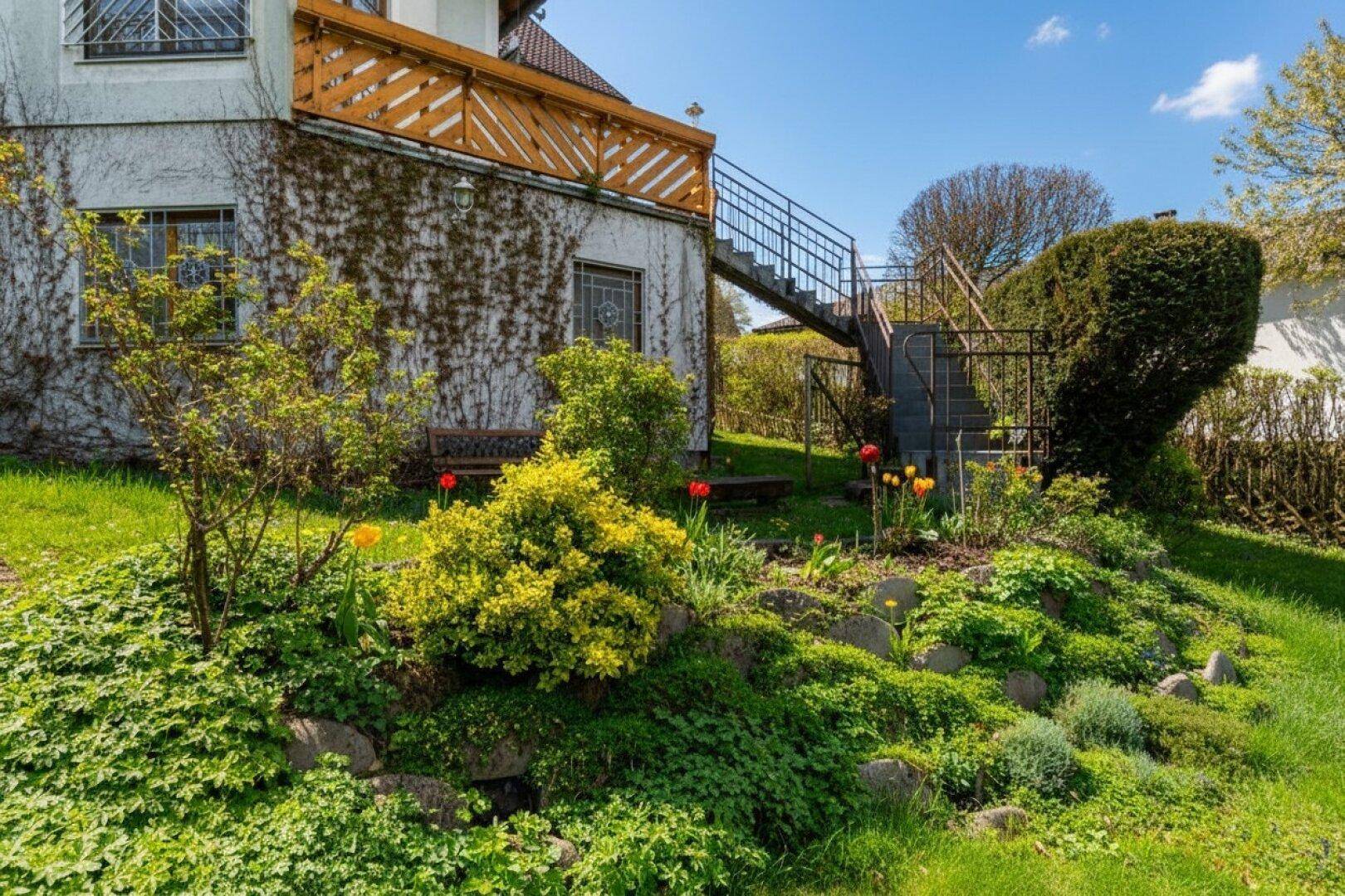 Terrassierter Gartenbereich mit Blumenbeeten und Außentreppe zum Haus.