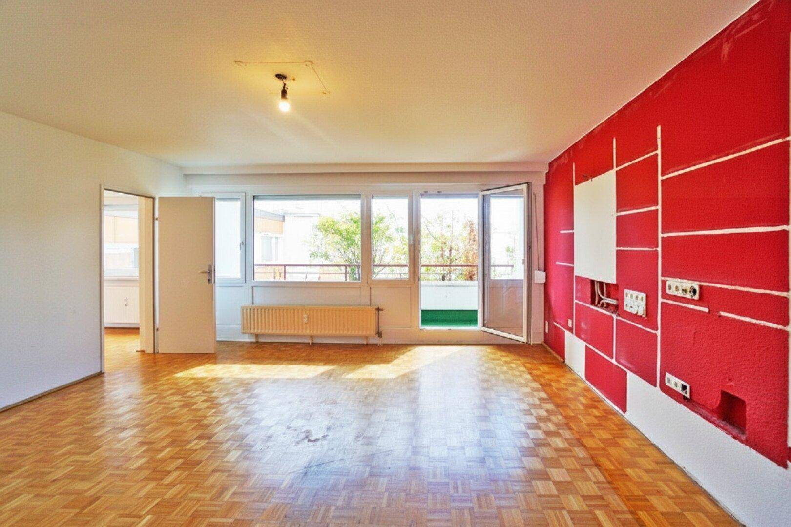Helles Wohnzimmer mit Parkettboden und großen Fenstern, die zum Balkon führen.