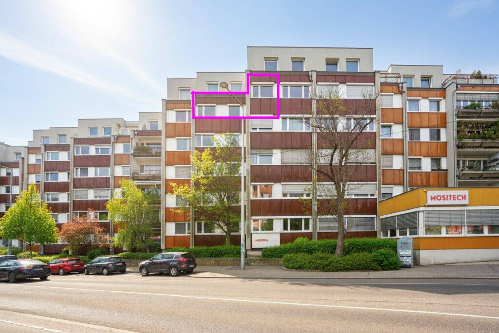 Ansicht der Wohnanlage von der Straße aus mit angrenzendem Geschäft und Parkplätzen.