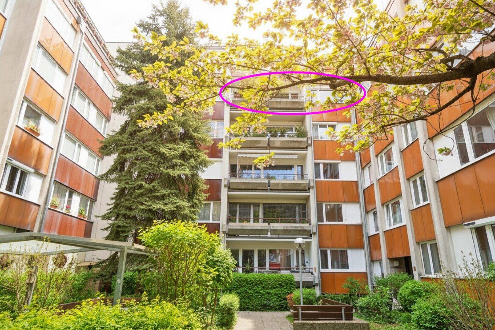 Fassade eines Apartmentgebäudes mit Balkonen und einem grünen Innenhof im Vordergrund.