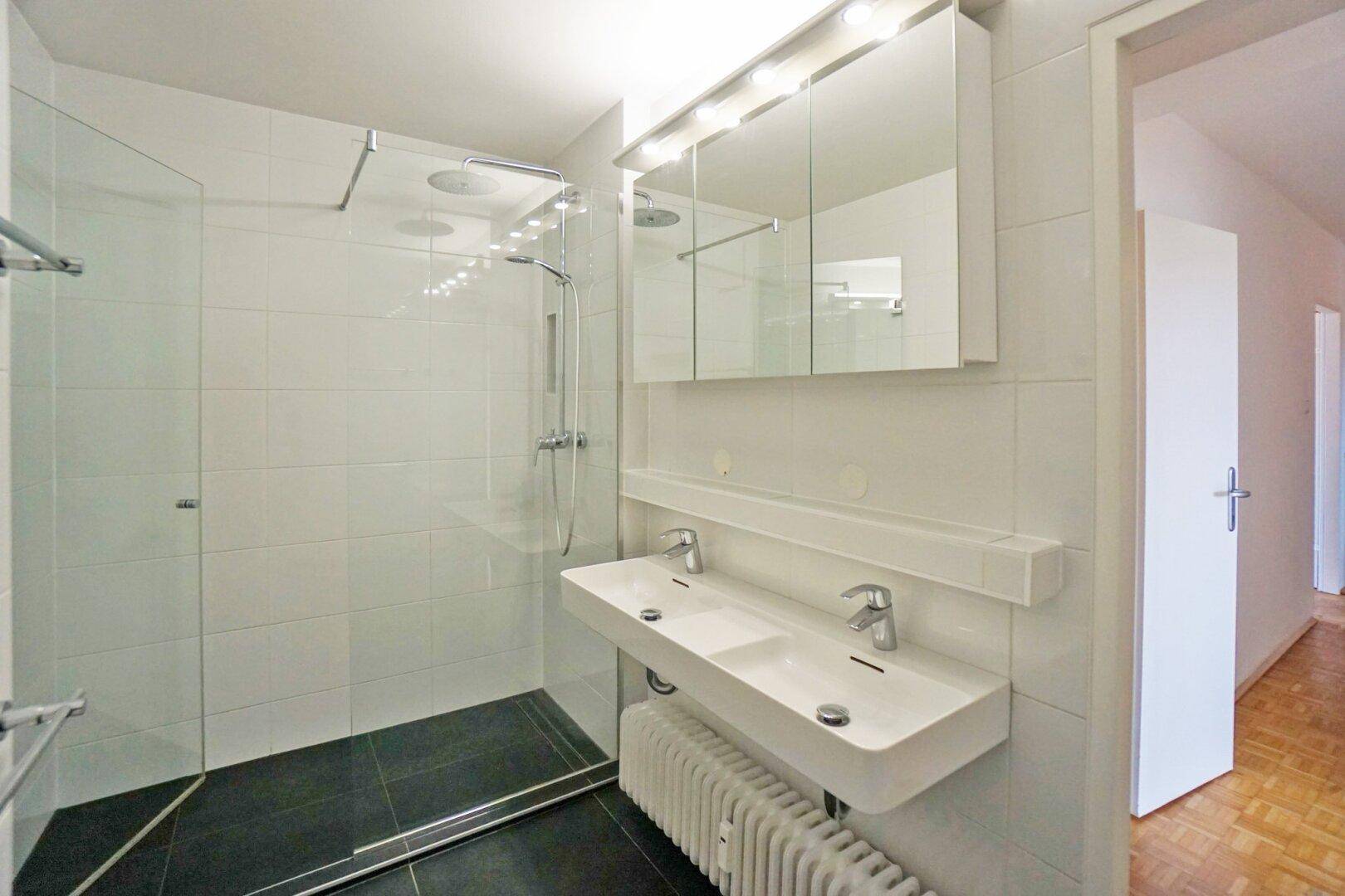 Modernes Badezimmer mit großer begehbarer Dusche, Doppelwaschbecken und weißen Fliesen.