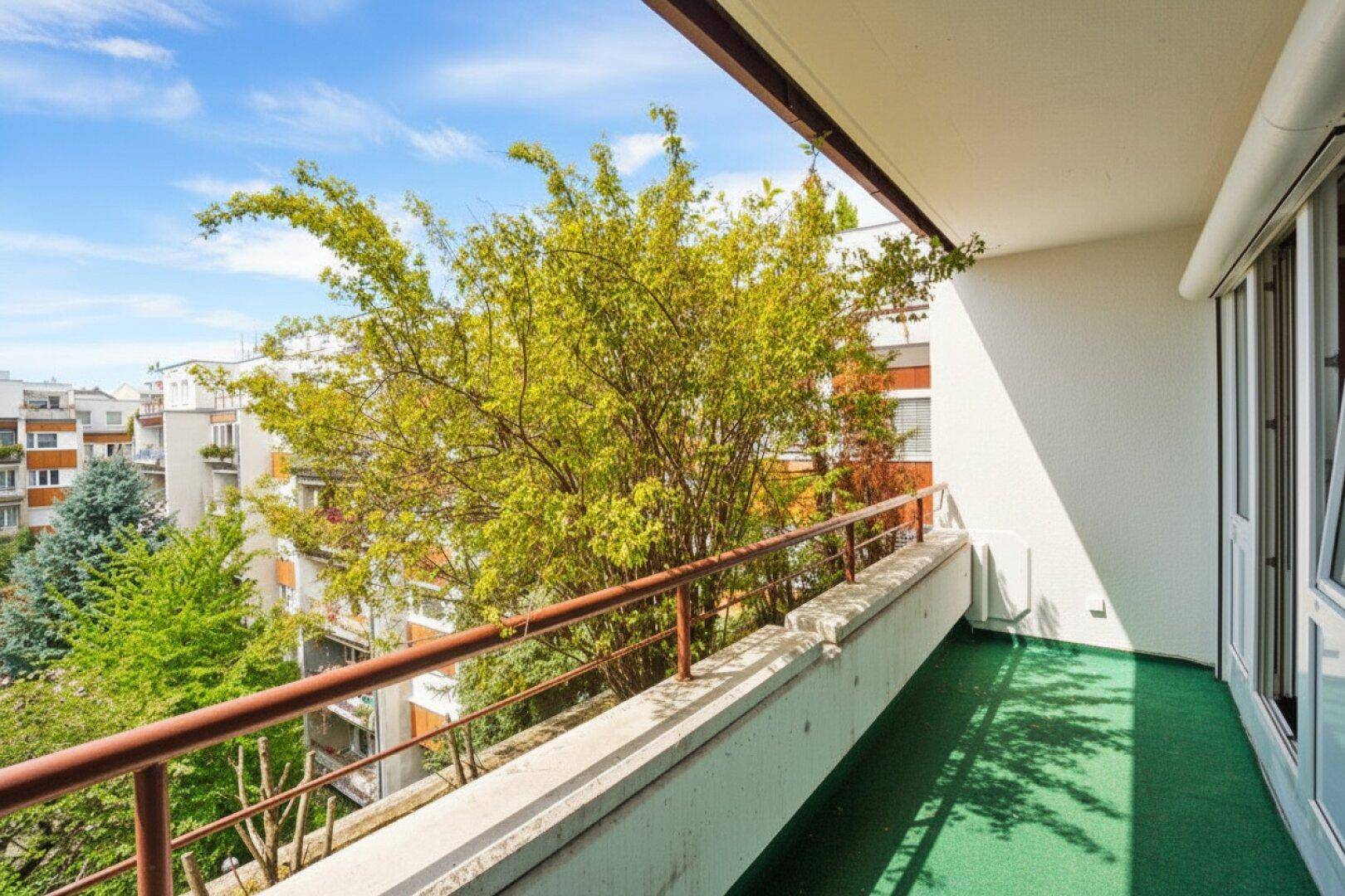 Geräumiger Balkon mit grünem Bodenbelag und Blick auf den begrünten Innenhof.