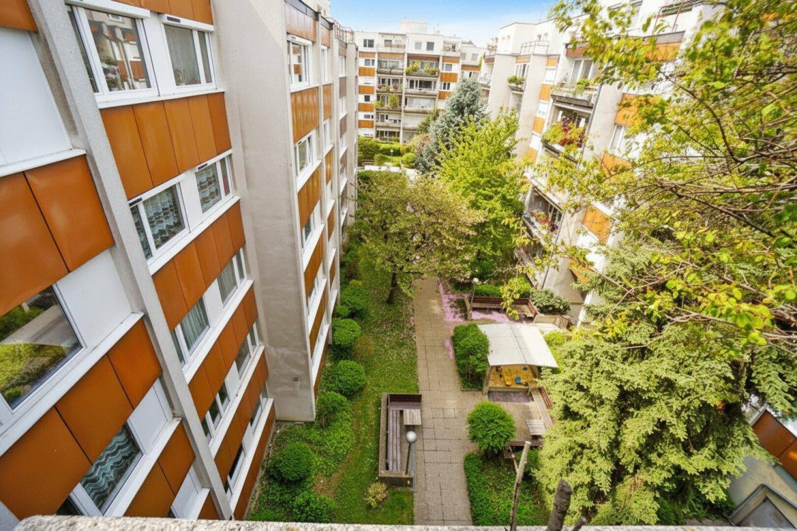 Blick von oben auf den gepflegten Innenhof der Wohnanlage mit Bäumen und Sitzgelegenheiten.