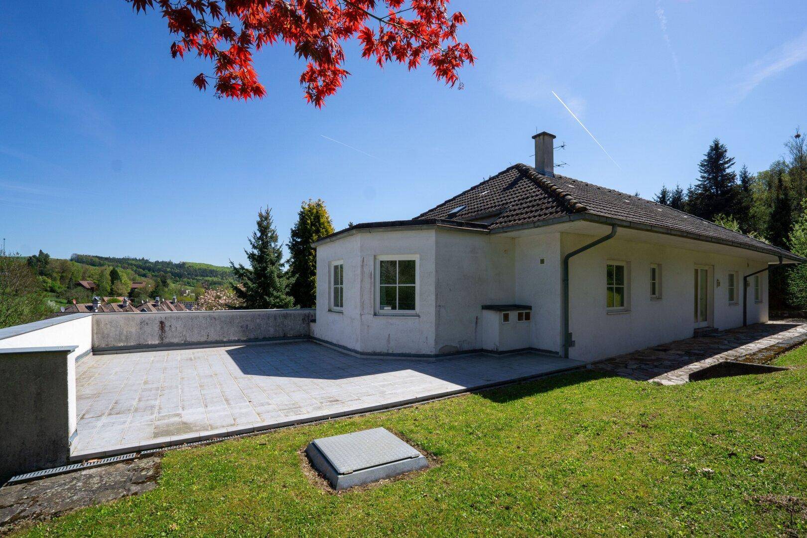 Seite des Hauses mit einer großen gepflasterten Terrasse und angrenzendem Rasen.
