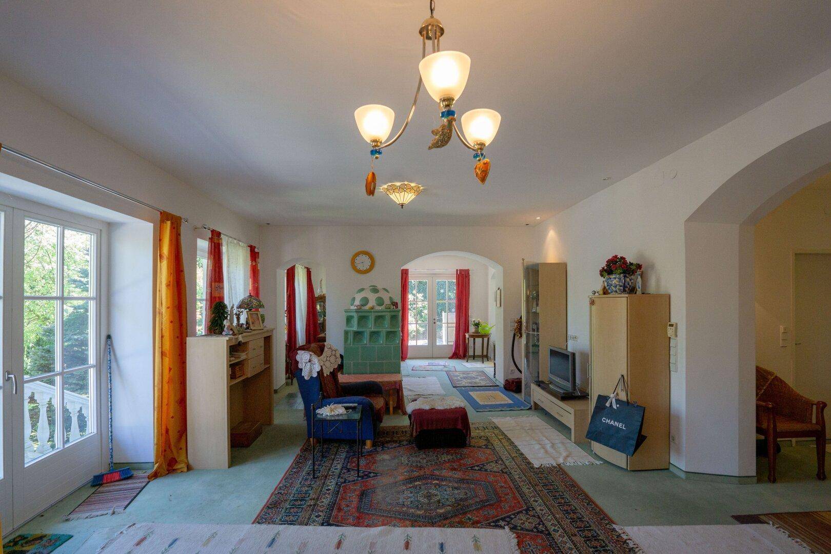Geräumiges Wohnzimmer mit traditionellem Kachelofen und Zugang zum Außenbereich.