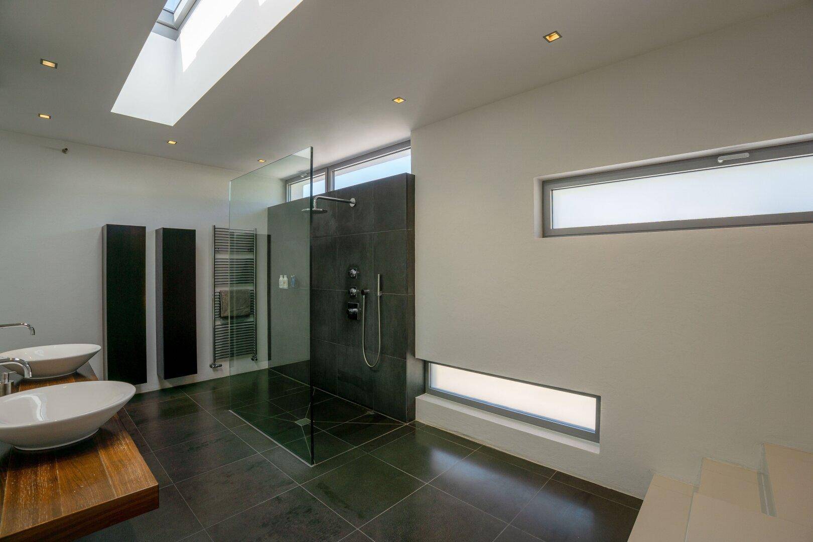 Geräumiges Badezimmer mit begehbarer Dusche, modernen Fliesen und Oberlicht für natürliches Licht.