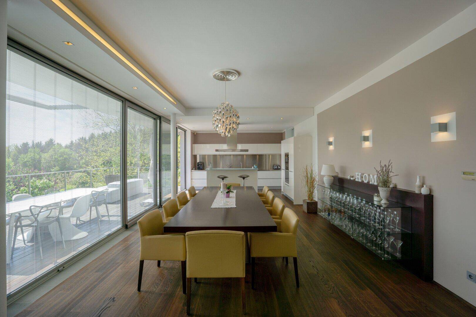 Geräumiger Essbereich mit langem Holztisch, gelben Stühlen und offener Küche mit Terrassenzugang.