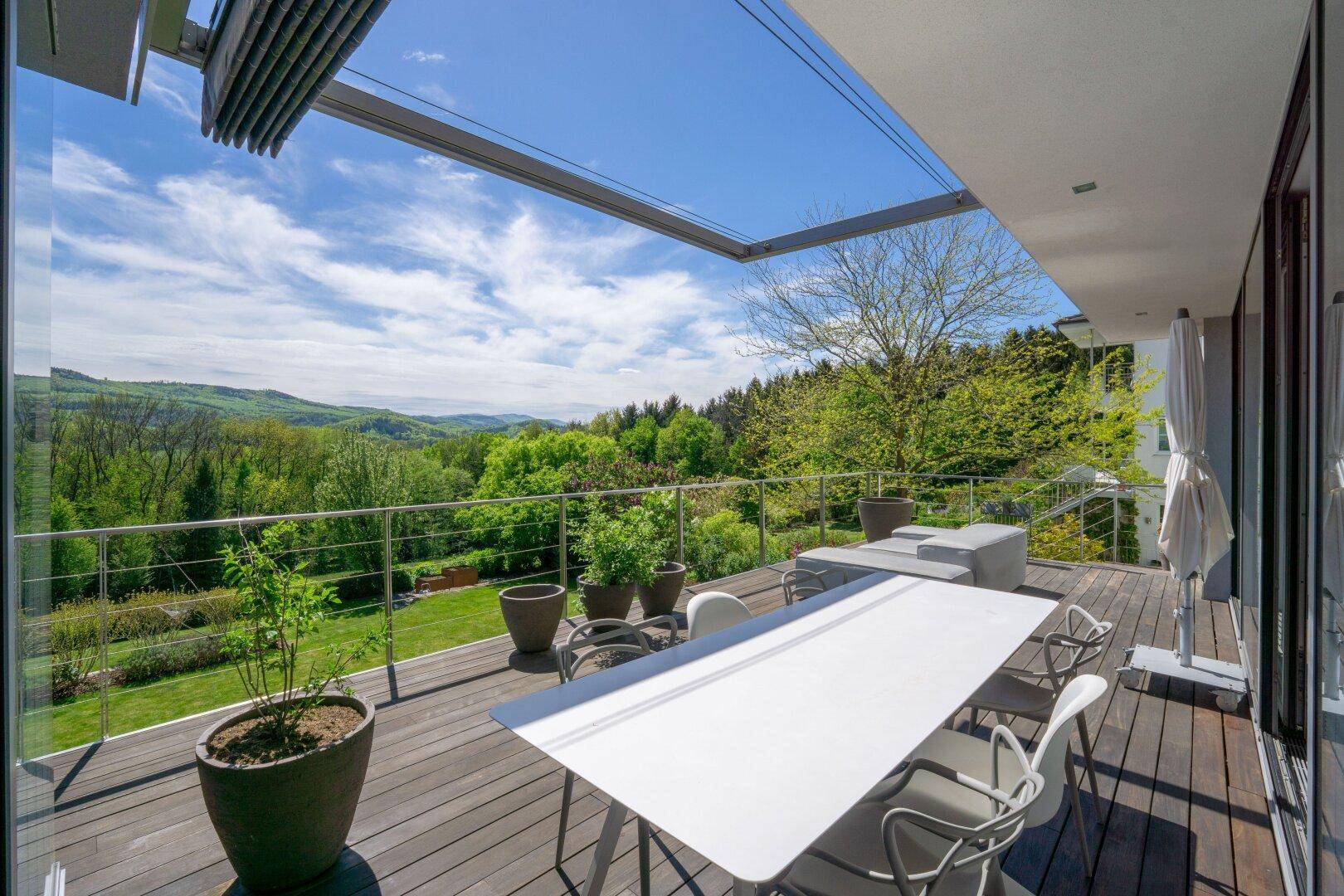 Große Holzterrasse mit Esstisch, Sonnenliegen und weitem Blick über die grüne Landschaft.