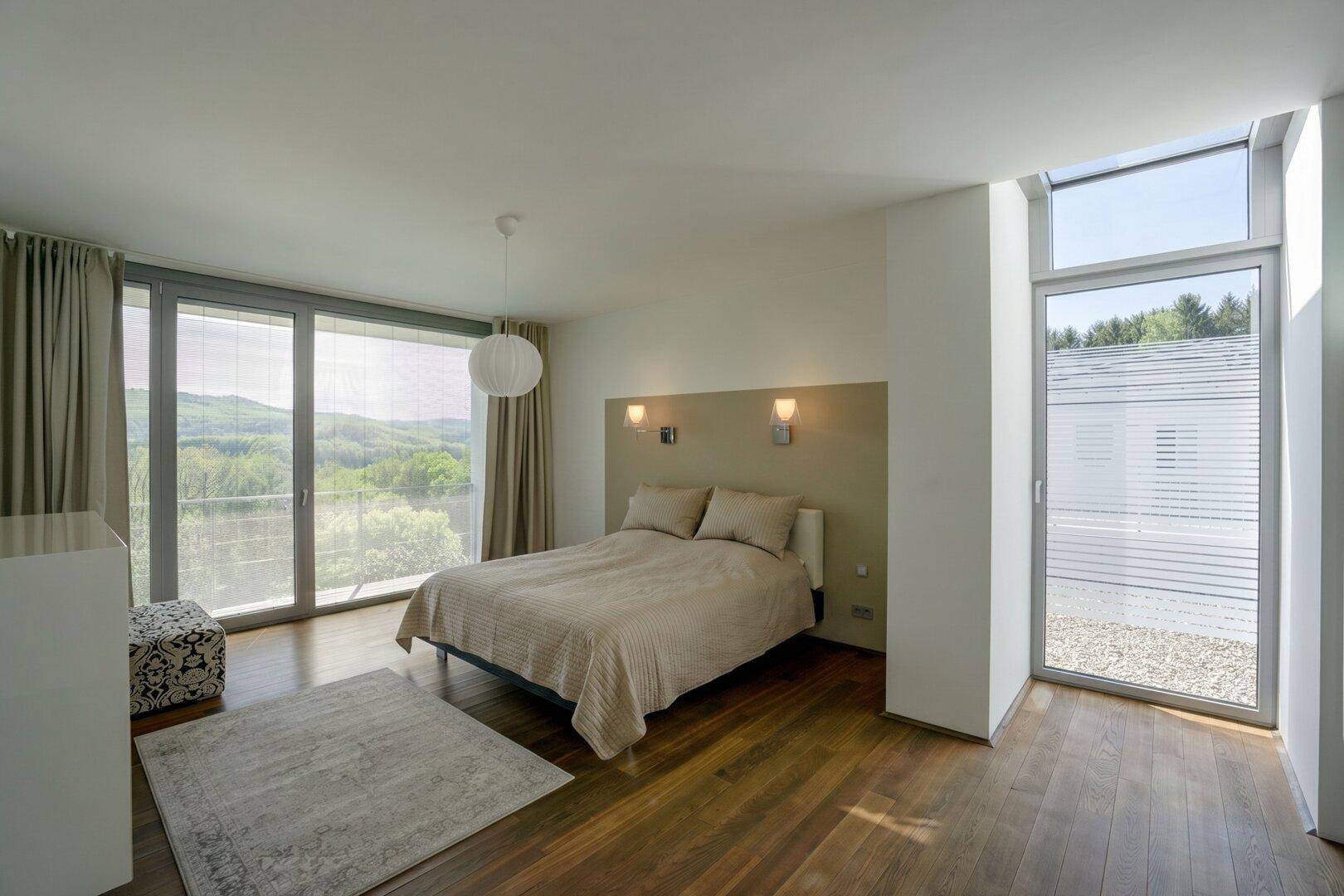 Helles Schlafzimmer mit Doppelbett, Holzboden und großen Fenstern mit Panoramablick.