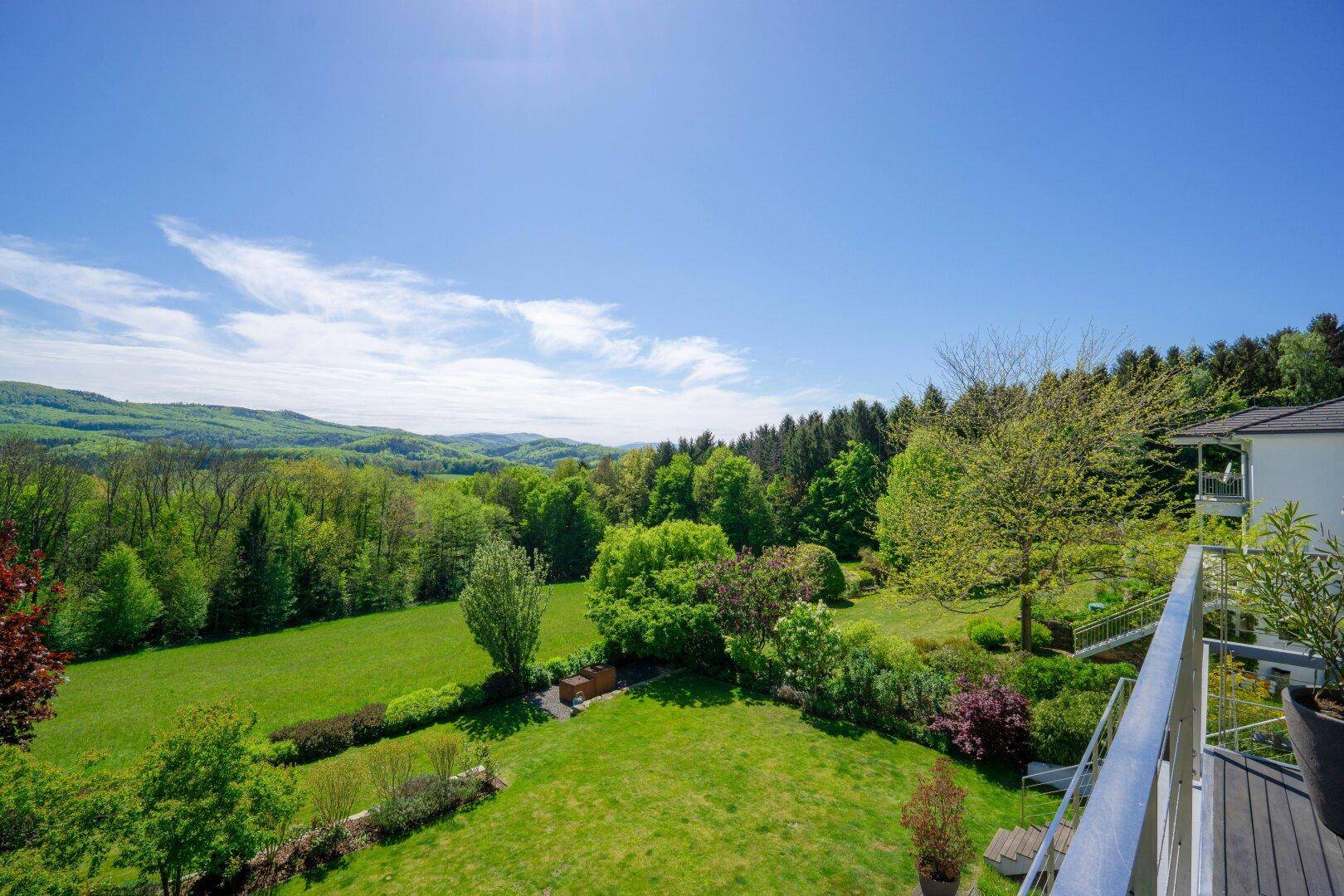 Panoramablick vom Balkon über die weitläufige grüne Landschaft und bewaldete Hügel.