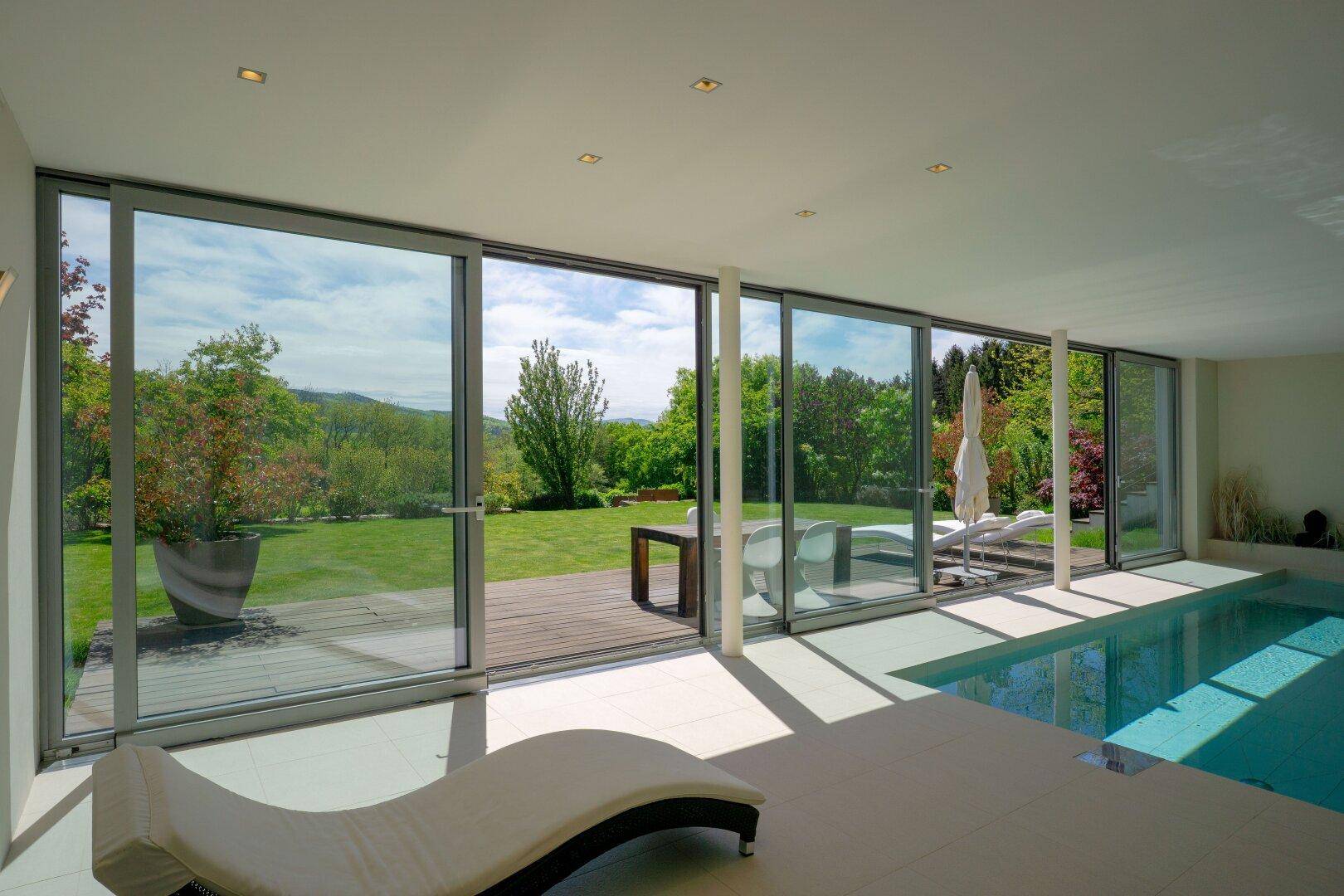 Innenpool mit Liegeflächen und Panoramablick auf den weitläufigen Garten und die Landschaft.