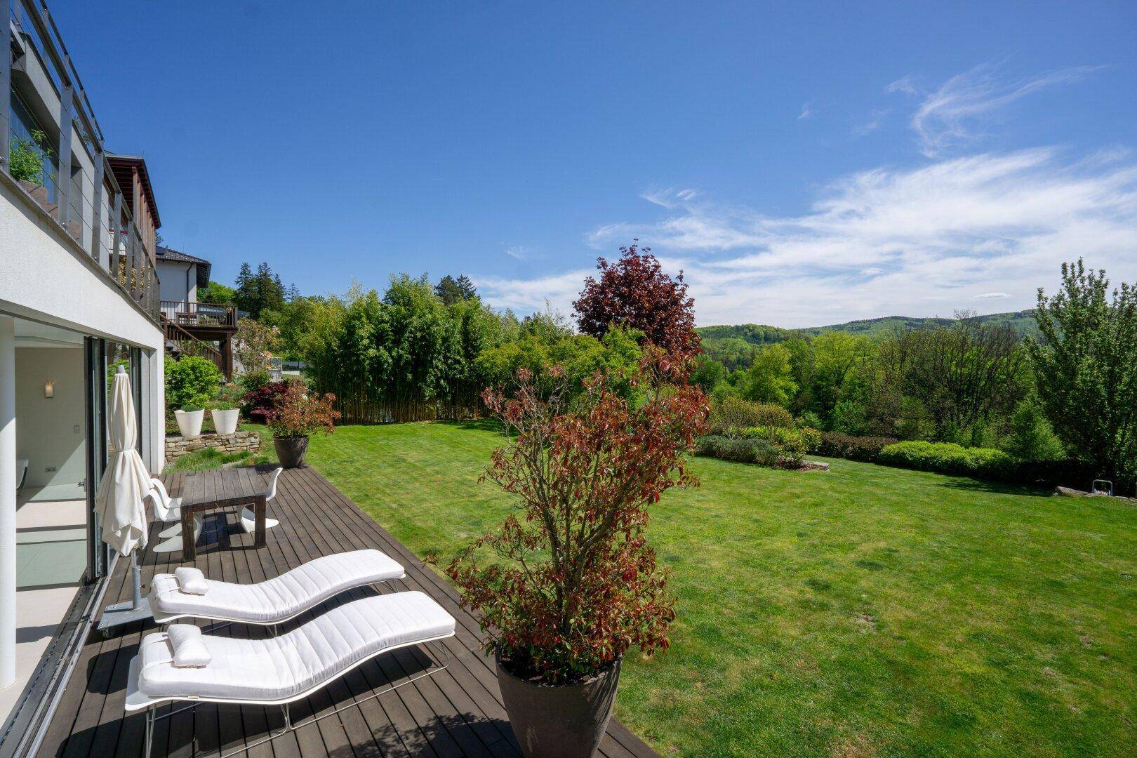 Sonniger Terrassenbereich mit Liegestühlen und Blick auf den weitläufigen Garten und die Natur.