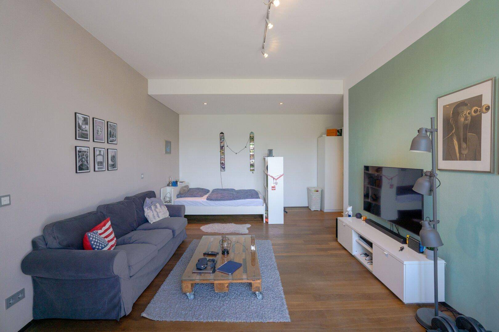 Gemütliches Wohnzimmer mit Sofa, Fernseher und Holzboden, teilweise als Schlafbereich genutzt.