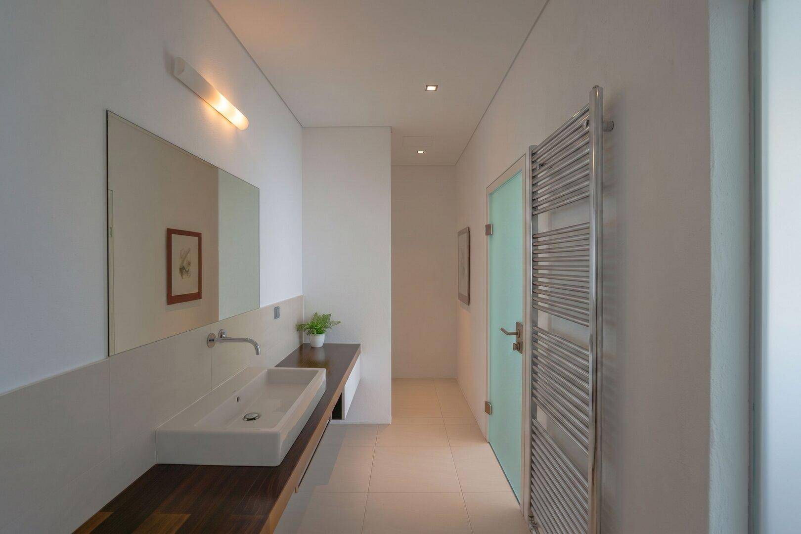 Modernes Badezimmer mit langem Einzelwaschbecken, großem Spiegel und beheiztem Handtuchhalter.