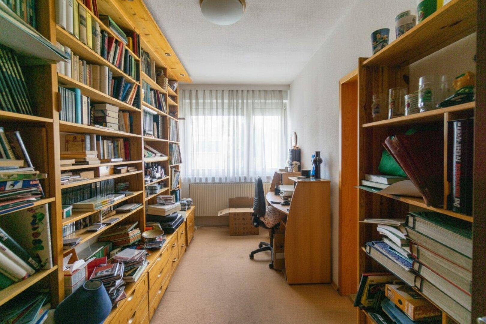 Arbeitszimmer mit raumhohen Bücherregalen, Schreibtisch und Fenster, ideal für Studierende.